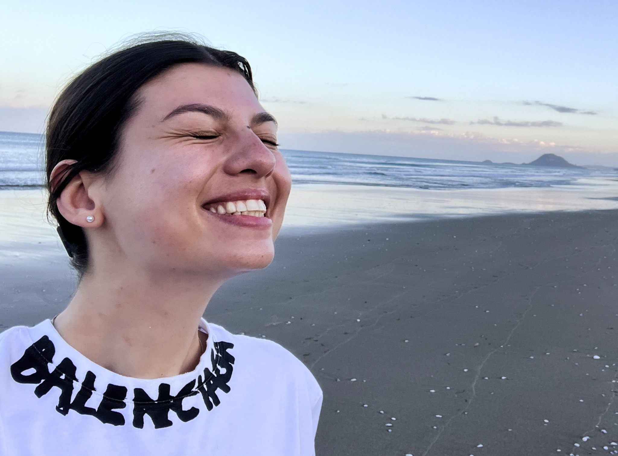 Danielle smiling on a beach at dusk, with the ocean and distant islands behind her